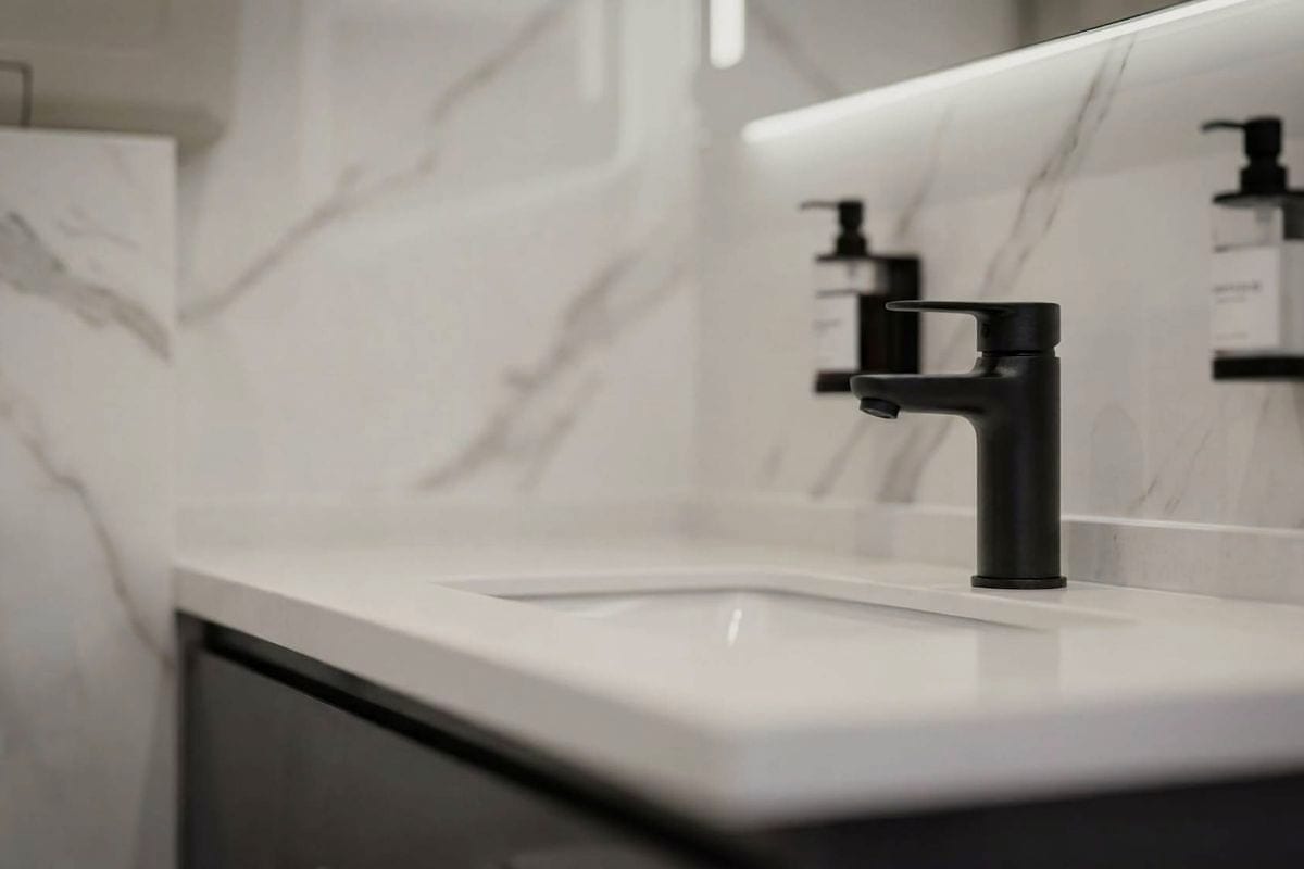 Plan de toilette en marbre, vasque encastrée et robinetterie noire.