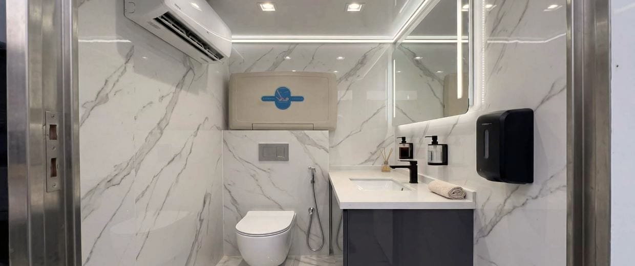 Intérieur d'une cabine : marbre, climatiseur mural, vasque et miroir rétroéclairé.